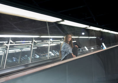 Woman sitting on escalator in city at night