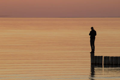 Silhouette man standing in sea against sky during sunset