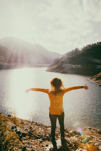 Rear view of man standing by lake against sky