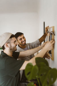 Happy gay couple helping each other while hanging frame on wall at home