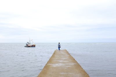 Woman standing on pier over sea against sky