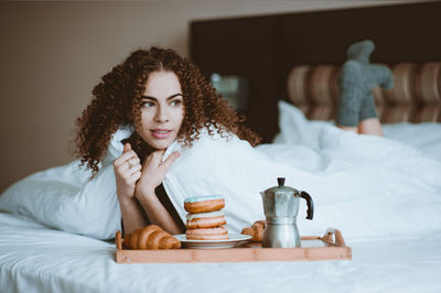 Young woman looking away while lying on bed