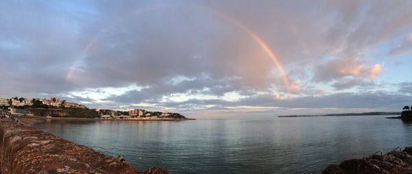 Scenic view of rainbow over sea against cloudy sky