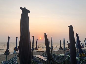 Closed umbrellas at shore of beach during sunset