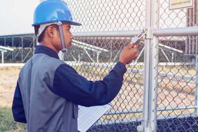 Male engineer opening padlock hanging from fence