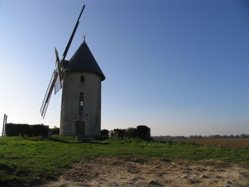 Tower on field by building against clear sky