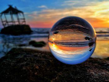 Close-up of crystal ball on rock at beach against sky during sunset