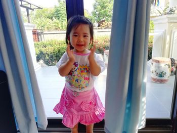 Portrait of cute baby girl standing against window