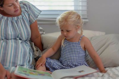 Woman sitting by daughter looking at picture book