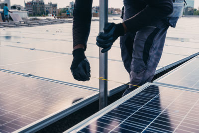 Workman in protective uniform installing modern solar panels on roof of industrial building