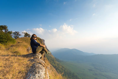 Side view full length of woman sitting on mountain against sky