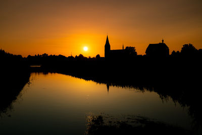 Reflection of silhouette buildings in lake during sunset