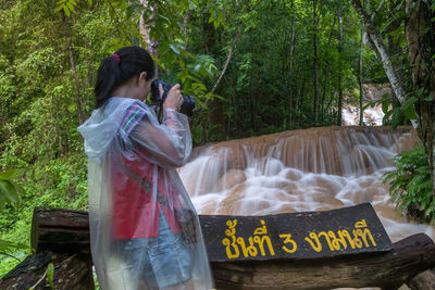 Woman photographing waterfall in forest