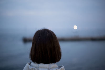 Rear view of woman standing against sea at dusk