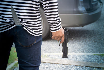 Midsection of man holding gun while standing outdoors