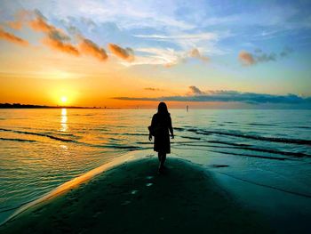 Rear view of silhouette woman looking at sea against dramatic sky during sunset