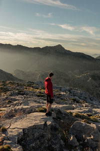 Rear view of man standing on rock against sky