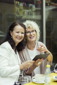 Happy senior women using digital tablet in outdoor cafe