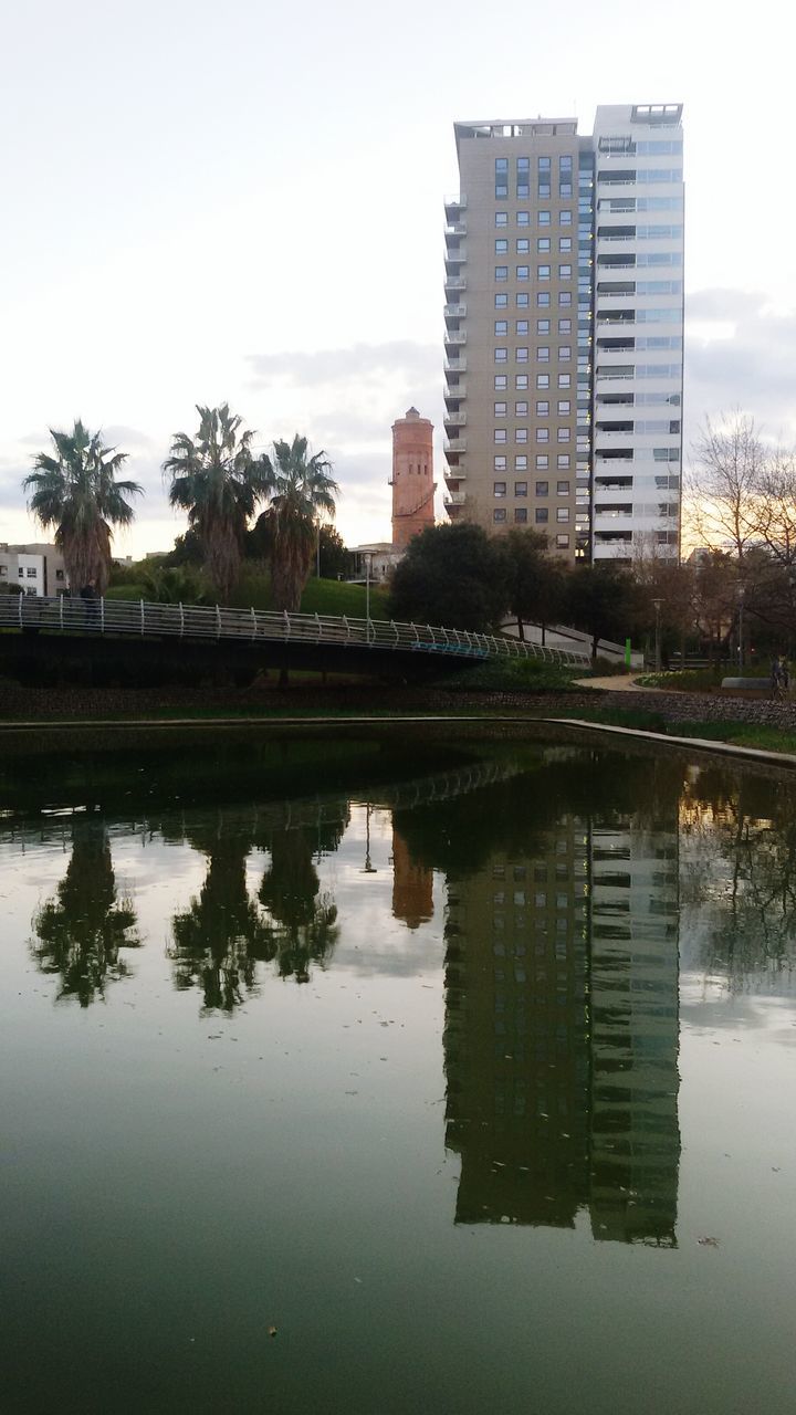 reflection, building exterior, architecture, built structure, water, tree, waterfront, sky, standing water, city, growth, lake, river, building, pond, clear sky, puddle, nature, outdoors, day