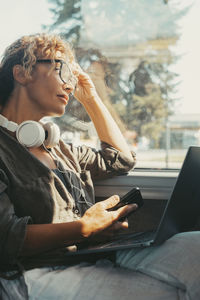 Side view of young man using mobile phone while sitting on sofa at home