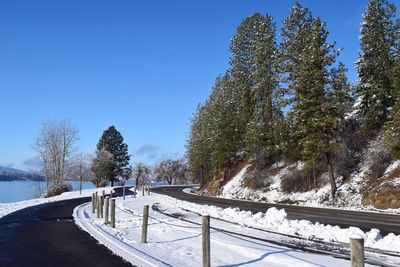 Snow covered road by trees against clear sky