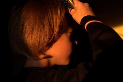 Close-up of boy combing hair in darkroom at home