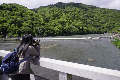 Woman photographing river against mountains