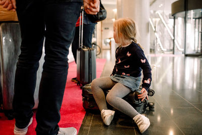 Girl sitting on suitcase with family standing at reception in hotel