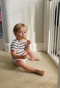 Portrait of cute baby boy with spoon sitting on carpet at home