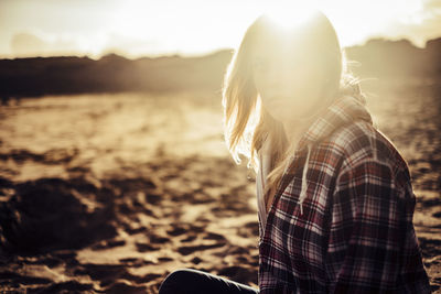 Young woman sitting at beach during sunset