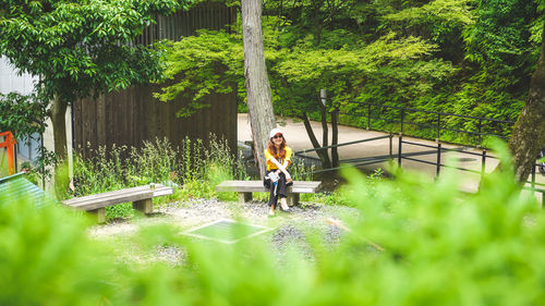 Portrait of young woman sitting on plants against trees
