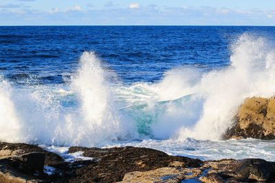 Waves splashing on rocks at shore against sky