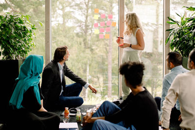 Businesswoman explaining male and female colleagues over adhesive notes during kick off meeting