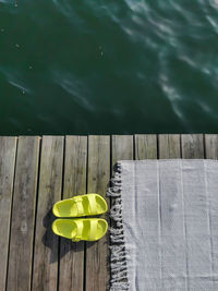 Neon sandals or flip flops  with beach rug on wooden floor, terrace beside deep lake water.