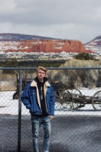 Portrait of man standing against fence during winter