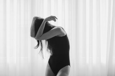 Woman hiding face while standing against curtain at home