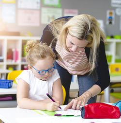 Teacher assisting student in studying at classroom