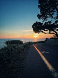 Road by trees against sky during sunset