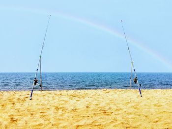 Fishing rods at beach against sky