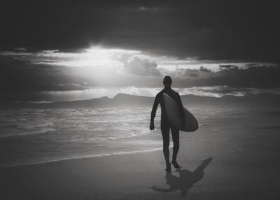 Rear view of man standing on beach against sky