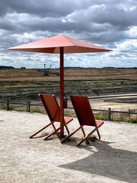 Empty chairs on beach against sky