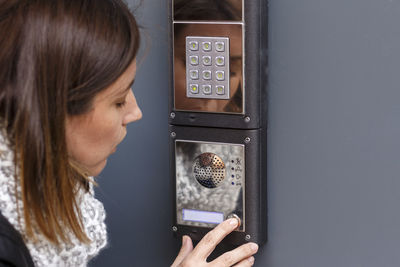 Close-up of woman using intercom on wall