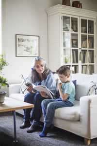 Grandmother and grandson reading picture book sitting on sofa at home