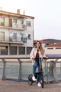 Ecologic transport for city. smiling young woman riding electric bicycle with city building behind