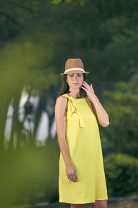 Thoughtful woman wearing hat standing against trees