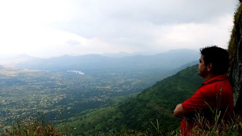 Side view of young man looking at mountains against sky