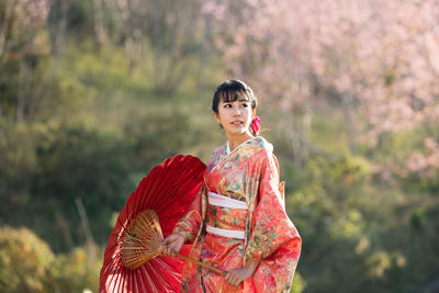 Woman with red umbrella standing against trees