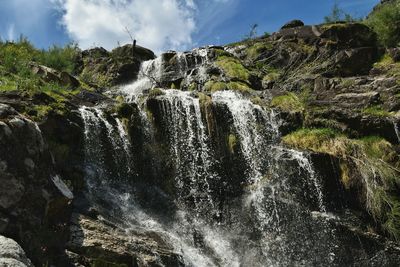 Low angle view of waterfall and mountain against sky