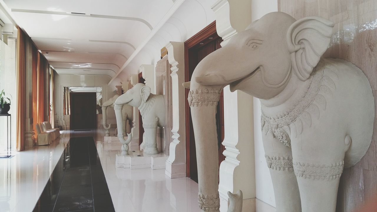 indoors, architecture, built structure, corridor, art and craft, architectural column, in a row, art, ceiling, human representation, creativity, no people, hanging, column, day, interior, building, statue, wall - building feature, door