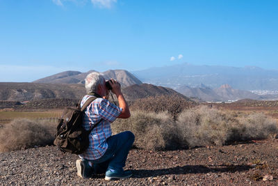 Rear view of man sitting on mountain against sky